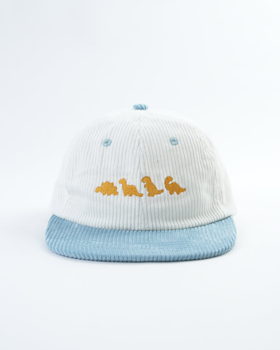White knit dino nugget hat with light-blue pom-pom, blue brim, yellow dino patch