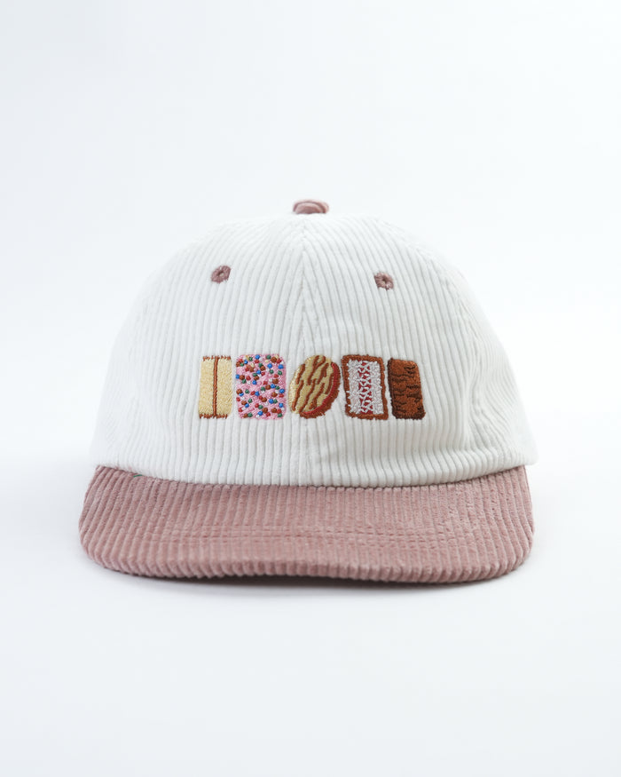 White ribbed cap with mauve brim and embroidered “Aussie Biscuits” lettering
